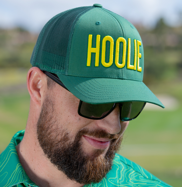 Men's Hoolie Garden City Bold Golf Trucker Hat with green 3D HOOLIE logo embroidery, yellow accents, and mesh back.