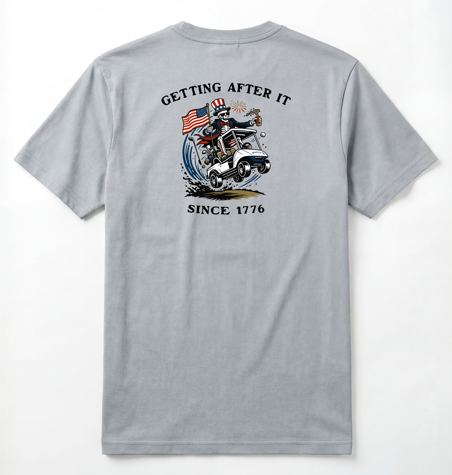 Back of Light gray T-shirt with Uncle Sam Skeleton Character in a Golf Cart carrying an American Flag with Text surrounding that says Getting After it Since 1776