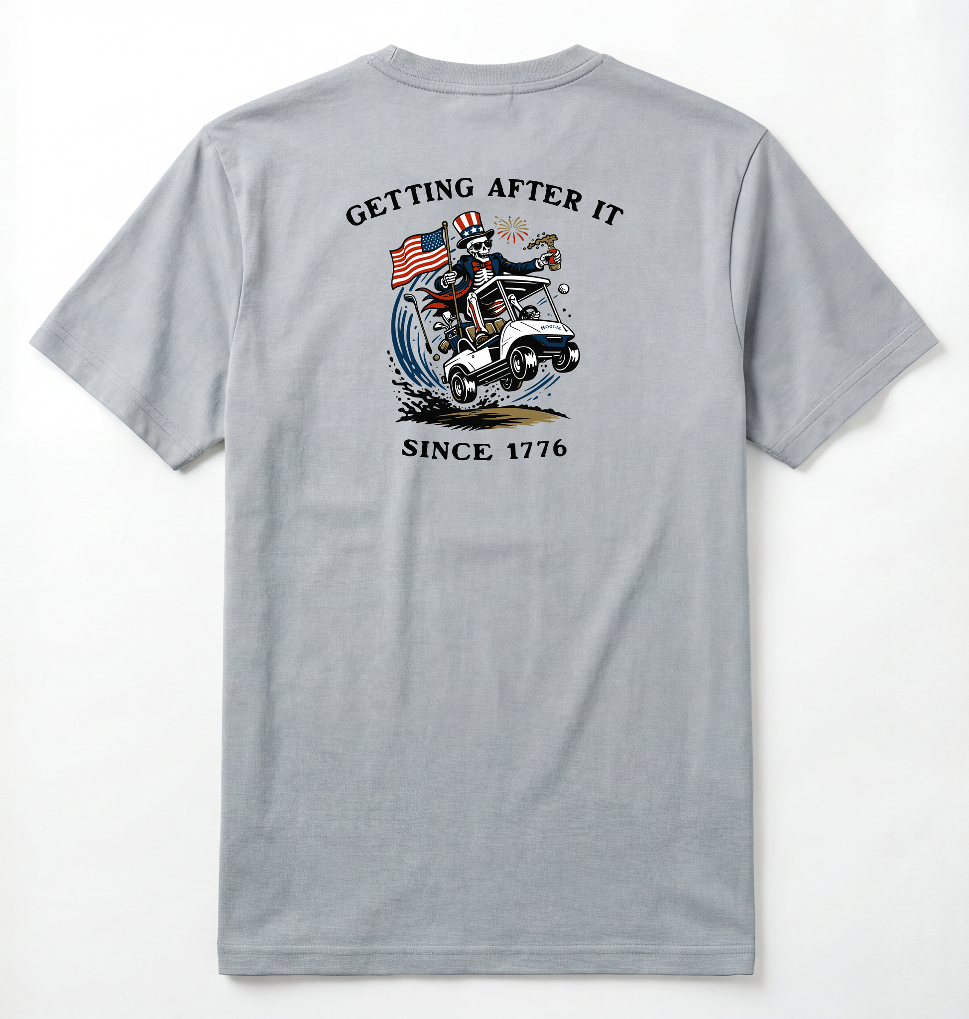 Back of Light gray T-shirt with Uncle Sam Skeleton Character in a Golf Cart carrying an American Flag with Text surrounding that says Getting After it Since 1776