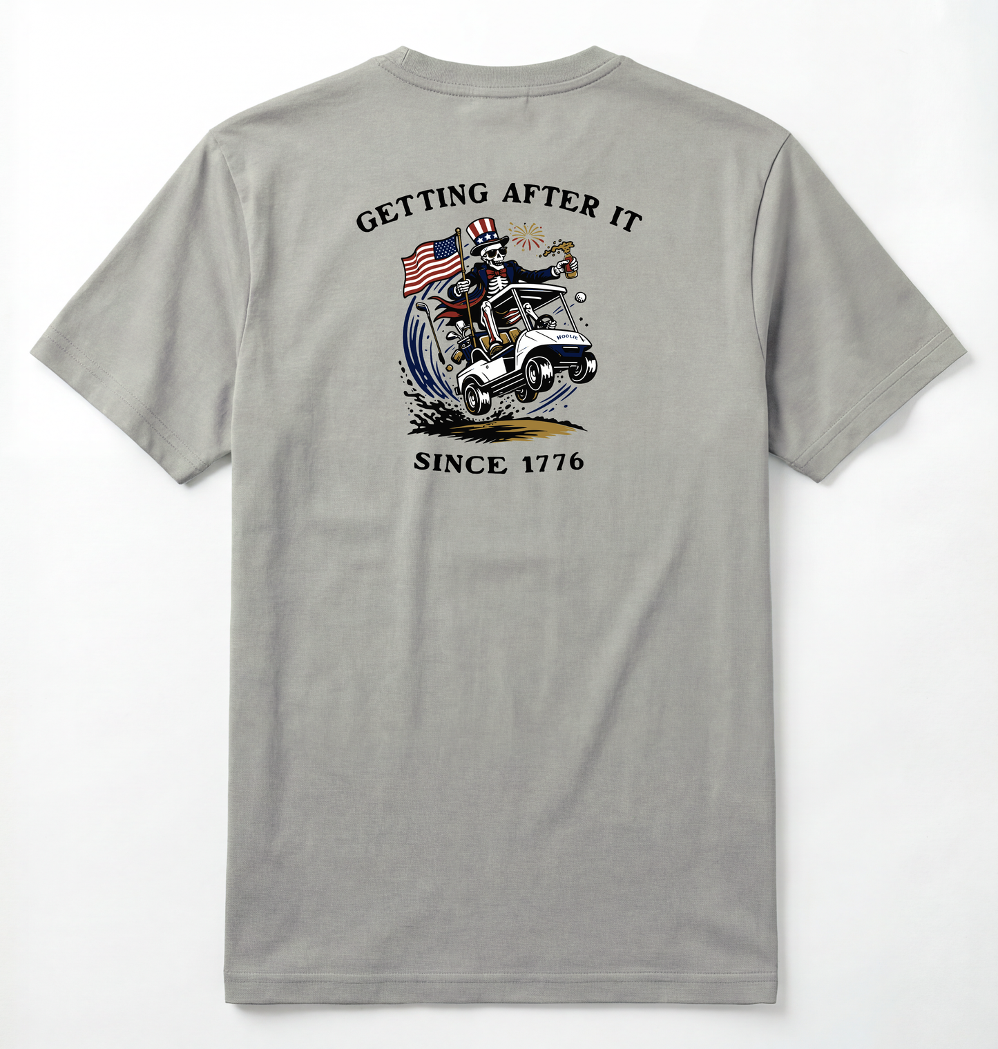 Back of Light gray T-shirt with Uncle Sam Skeleton Character in a Golf Cart carrying an American Flag with Text surrounding that says Getting After it Since 1776